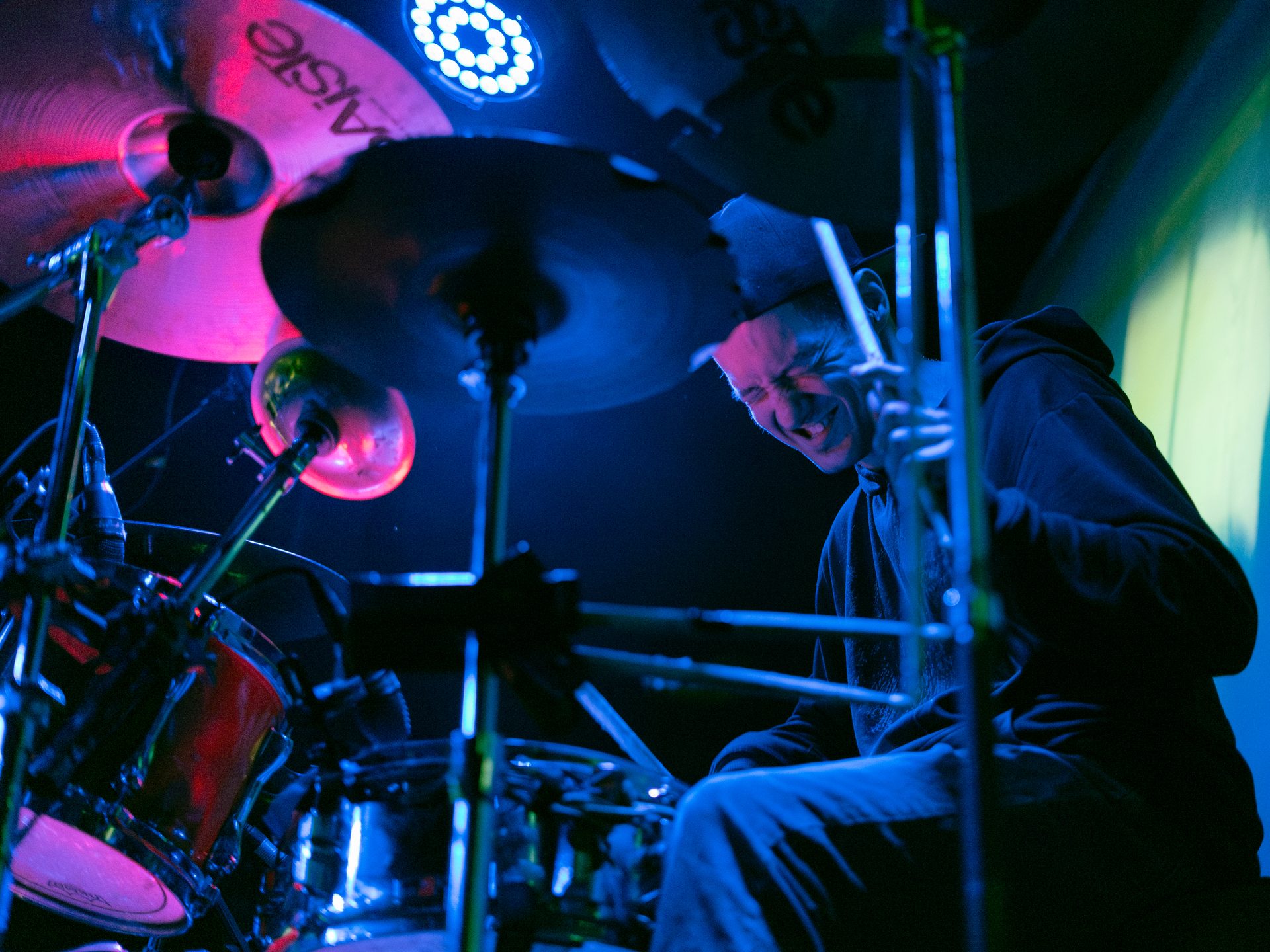 Drummer mid-performance under blue and magenta stage light